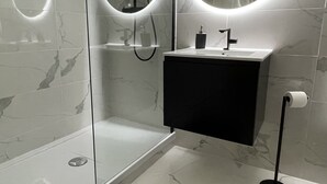 A modern bathroom with a glass-enclosed shower, a black vanity, and a round mirror with integrated lighting.