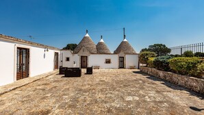 Un patio con un edificio blanco de tres techos cónicos, suelo de piedra y un muro de piedra en un lado.