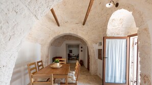 Un comedor rústico con una mesa y sillas de madera, techo abovedado de piedra y vista a otra habitación por un vano abierto.