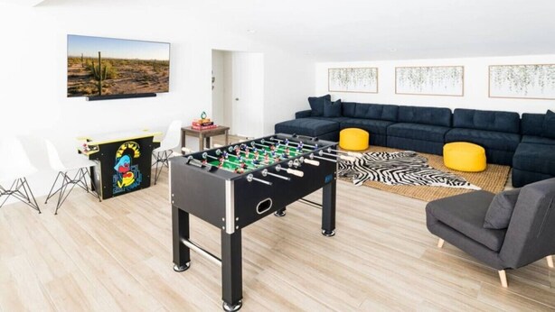 Una sala moderna con una mesa de fútbol, un conjunto de sofás y un cuadro en la pared.