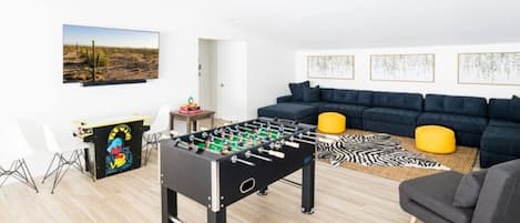 A modern living room with a foosball table, a sofa set, and a painting on the wall.