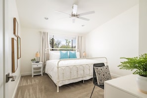 Ein Schlafzimmer mit einem Bett, Nachttischen, einem Deckenventilator und einem Fenster mit Vorhängen.
