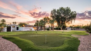 Un campo de golf con un club de campo, palmeras y un cielo al atardecer.