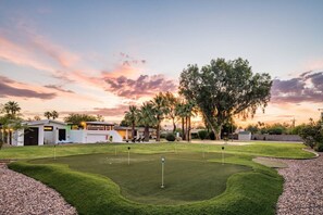 Ein Golfplatz mit Clubhaus, Palmen und einem Sonnenuntergangshimmel.