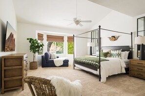A bedroom with a four-poster bed, a sofa, a small table, a lamp, and a ceiling fan.