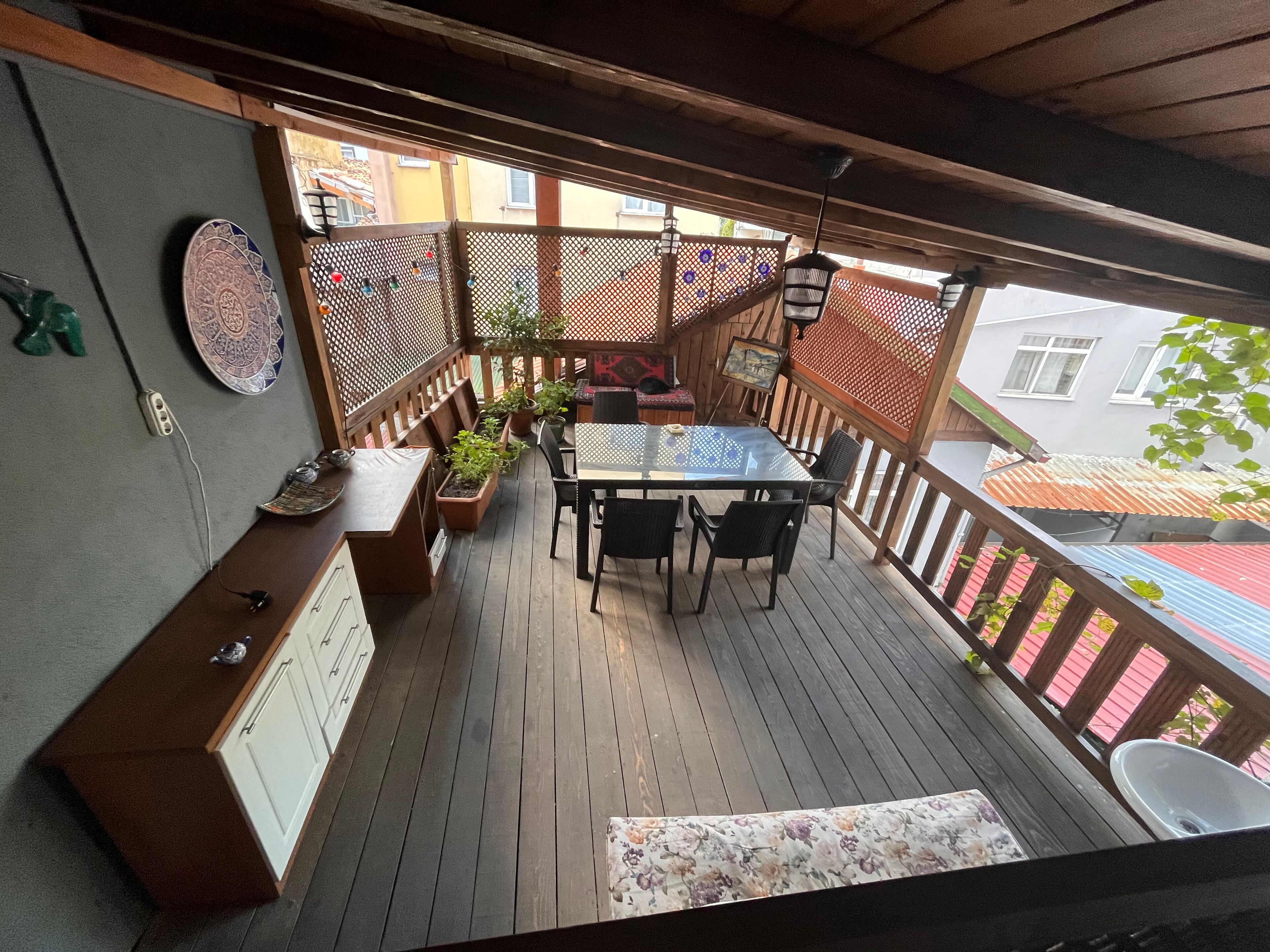 Una terraza de madera con una mesa, sillas, plantas en macetas y un banco.