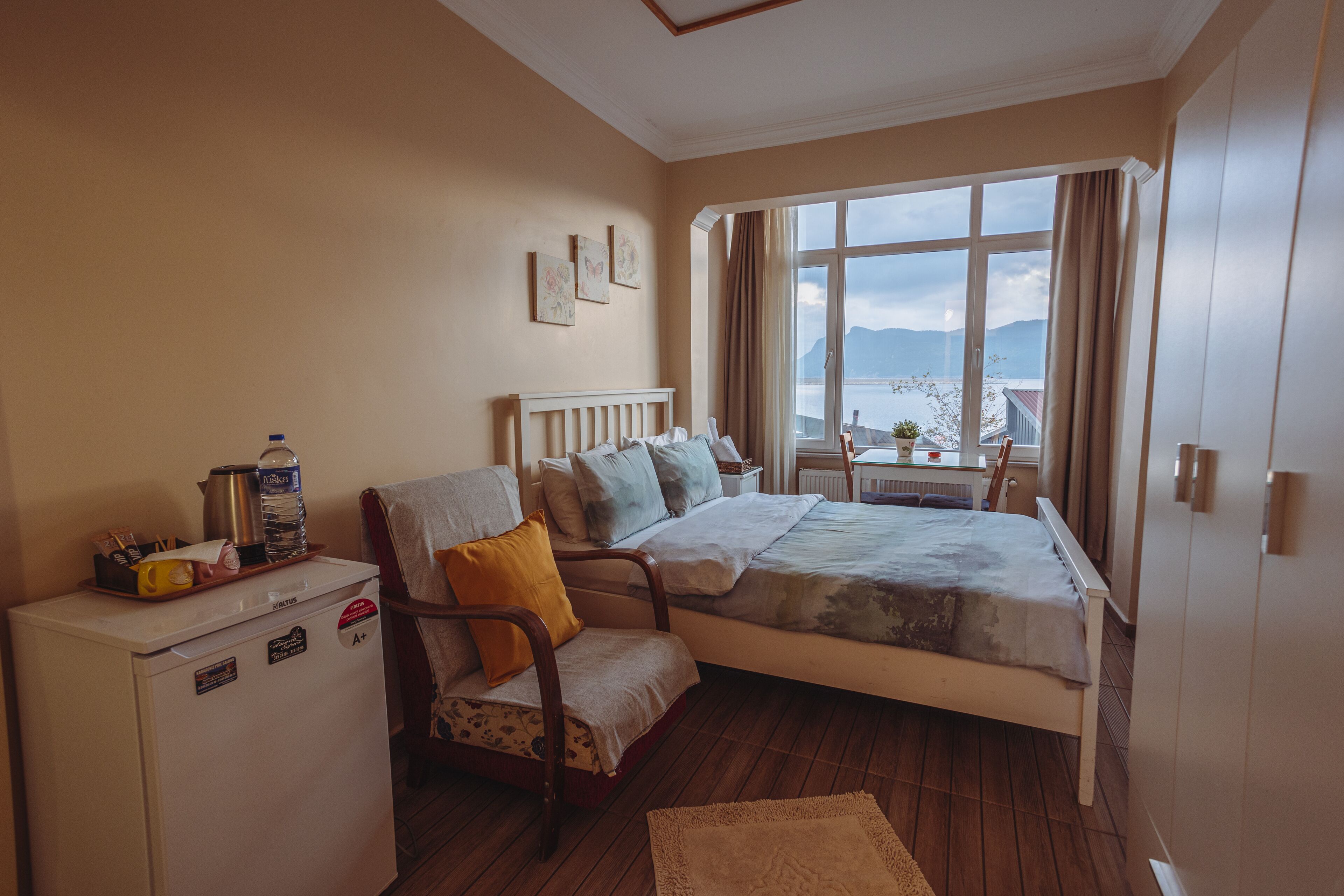 Un dormitorio con cama, una silla, una mesita y un refrigerador.