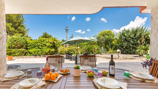An outdoor dining area with a table set for two, surrounded by greenery and a clear sky. - 3081 Villa Il Tulipano Verde by Barbarhouse (Putignano)
