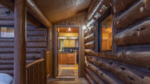 A log cabin interior with a wooden staircase leading to a kitchen area.