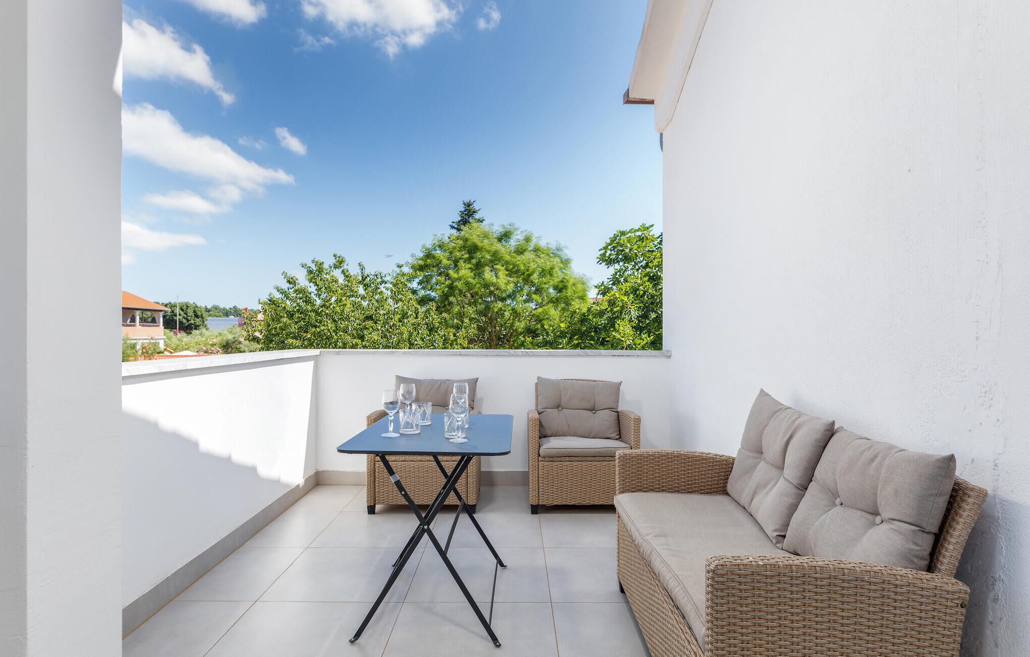 A balcony with a table and chairs, a view of trees and a body of water, and a white wall.