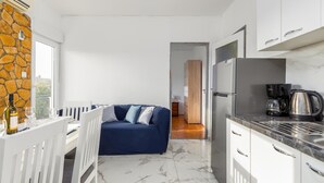 A modern kitchen with a marble countertop, a refrigerator, and a coffee maker. There is a blue sofa with cushions in the living area, and a stone wall with a window. - 3 bedroom stunning apartment in Medulin (Medulin)