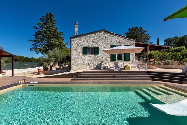 Una casa de piedra con piscina, zona de estar al aire libre y escalones que llevan a una terraza.