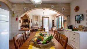 Un comedor con una mesa dispuesta para dos, una cocina con armarios blancos y una pared de piedra.