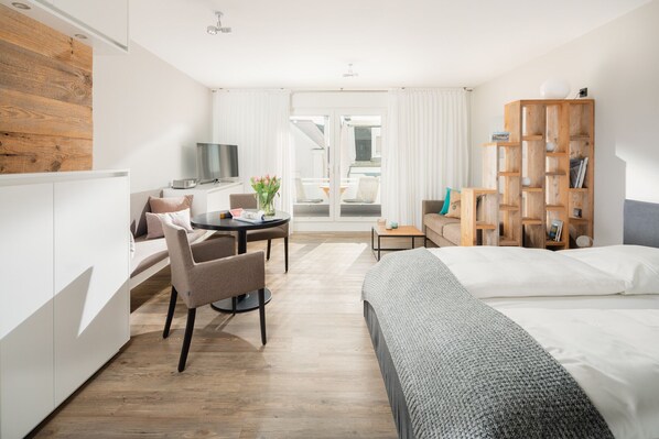A modern hotel room with a bed, a desk with a chair, a TV, and a bookshelf.