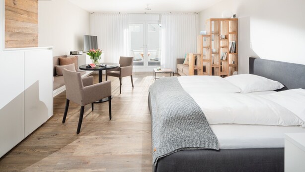 A modern hotel room with a bed, a desk, a chair, and a bookshelf. - // Strandzeit 13 // (Norderney)