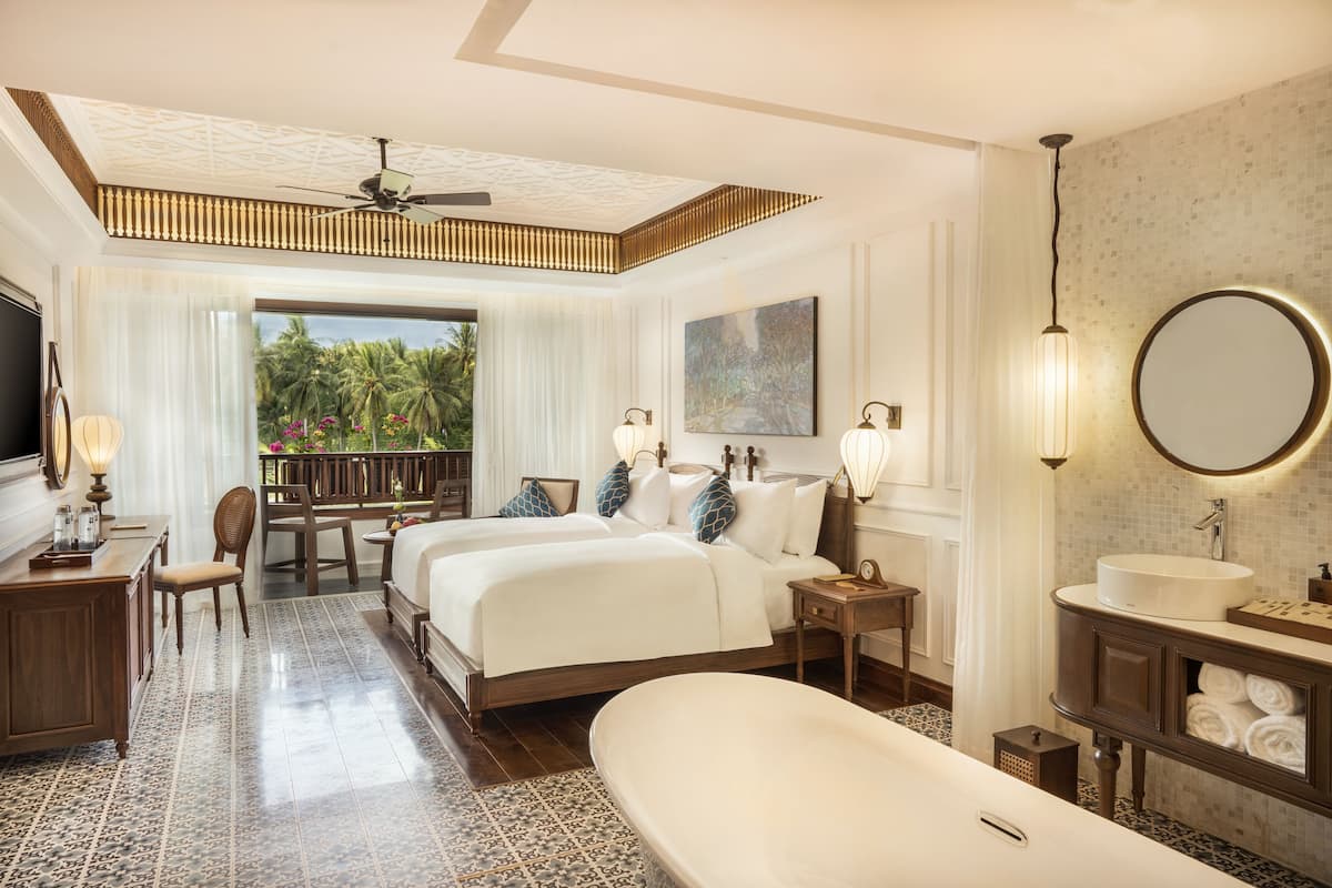 A hotel room with two beds, a large bathtub, a balcony with a view of palm trees, and a modern bathroom.