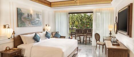 A spacious bedroom with a large bed, a ceiling fan, a painting, and a view of palm trees through the window.