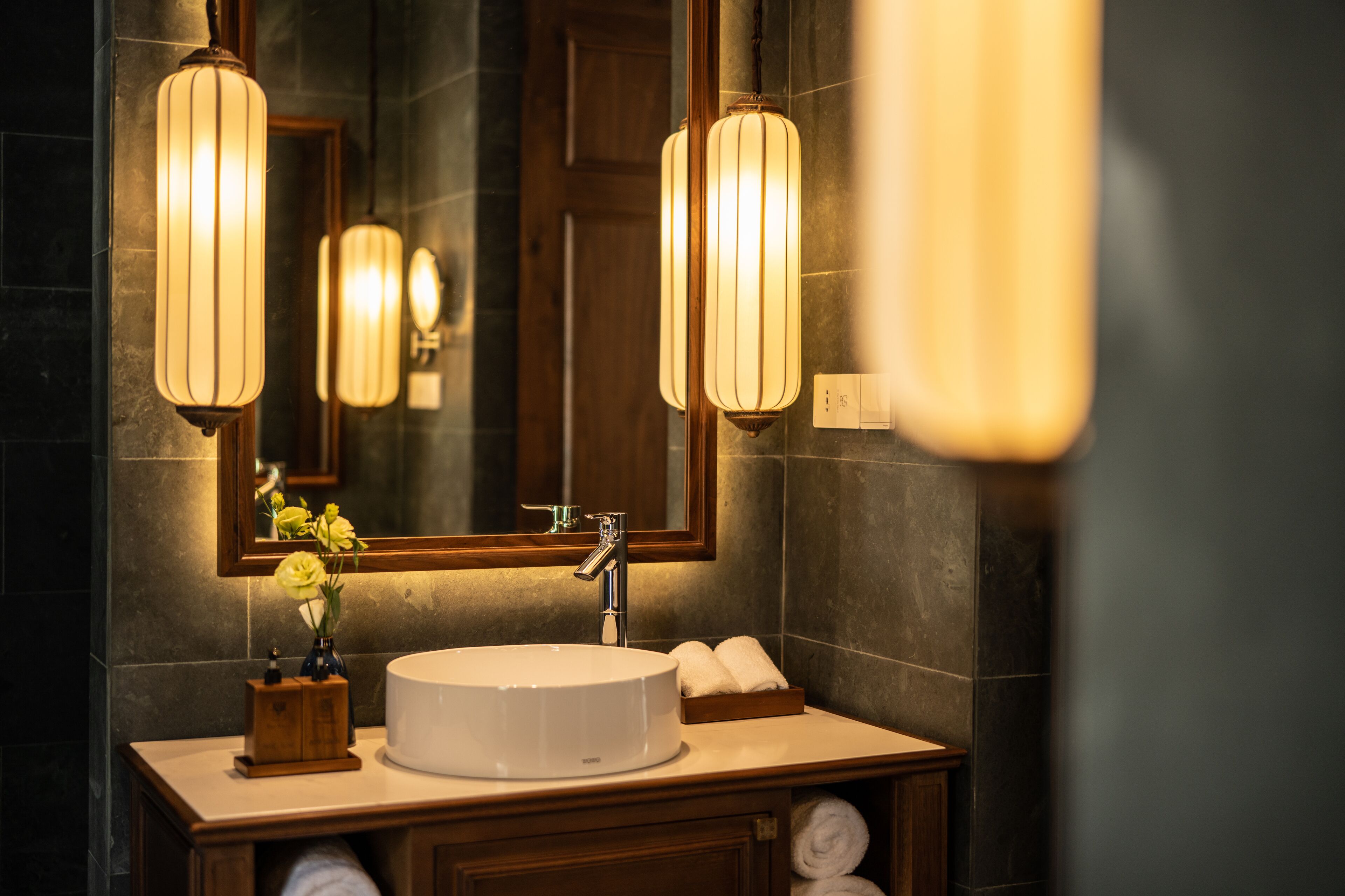 A bathroom with a round sink, wooden vanity, and two wall-mounted lights.