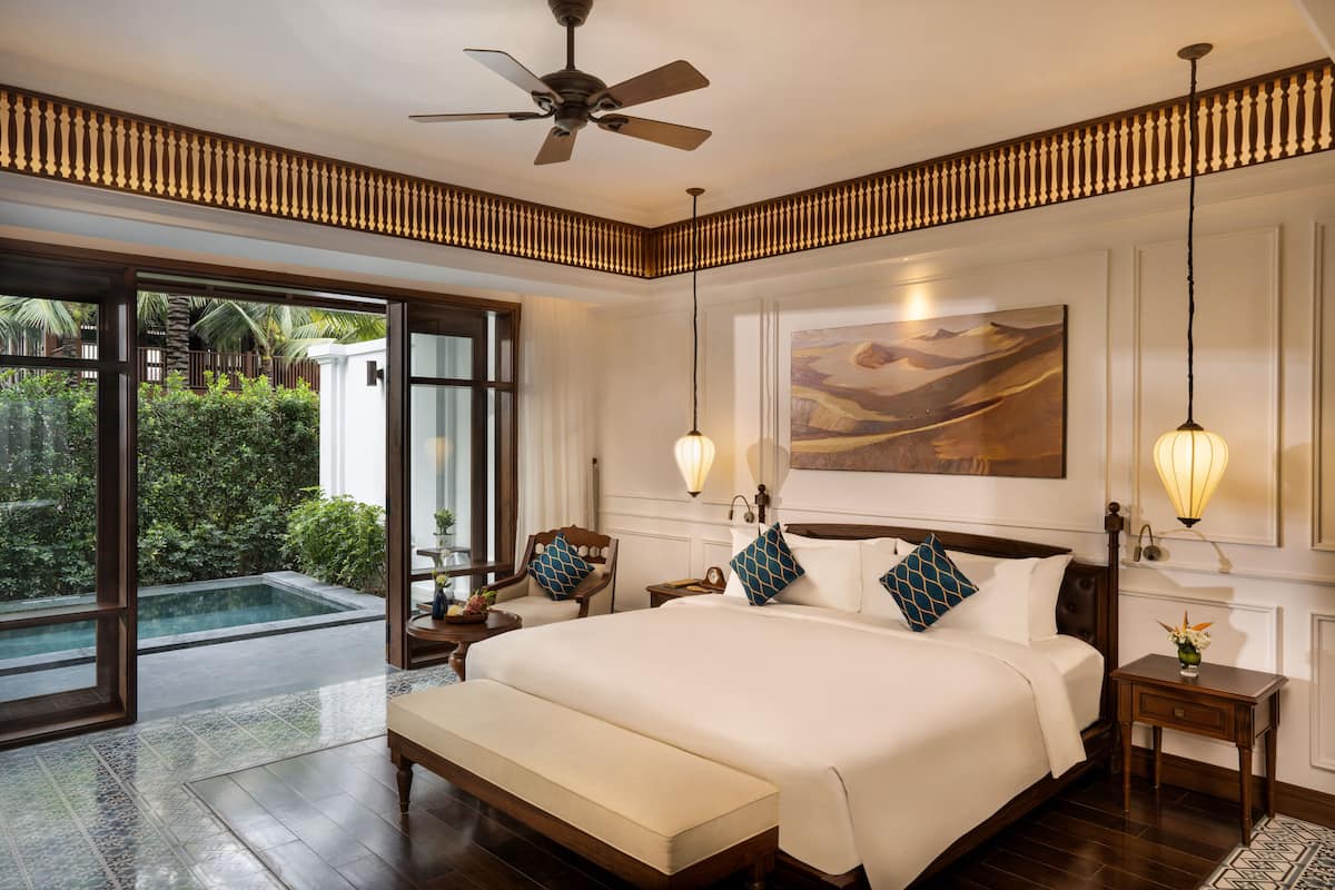 A spacious bedroom with a large bed, a ceiling fan, a nightstand, a bedside table, and a view of a swimming pool.
