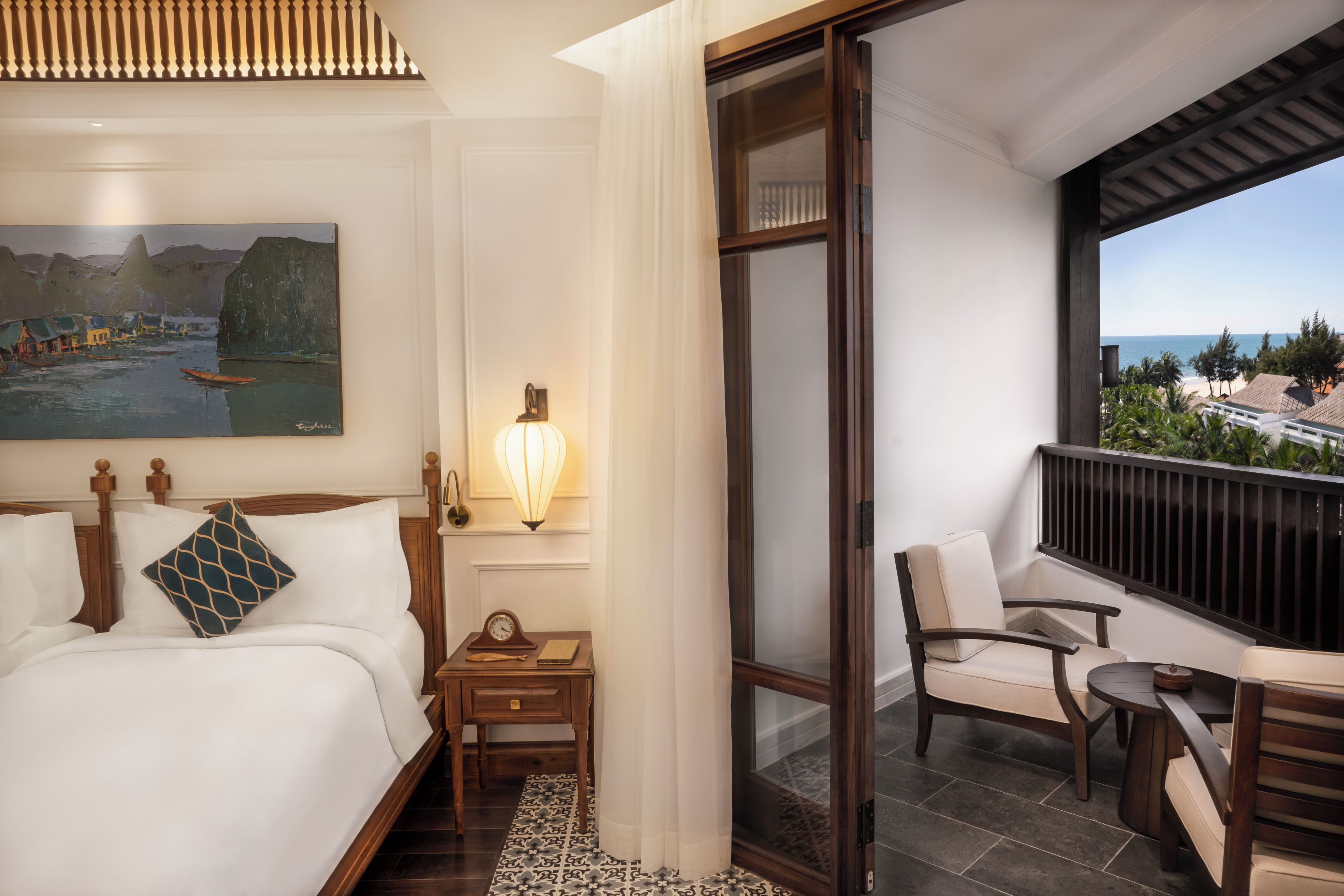 Habitación de hotel con cama, mesita de noche, lámpara, silla y vista a la playa.