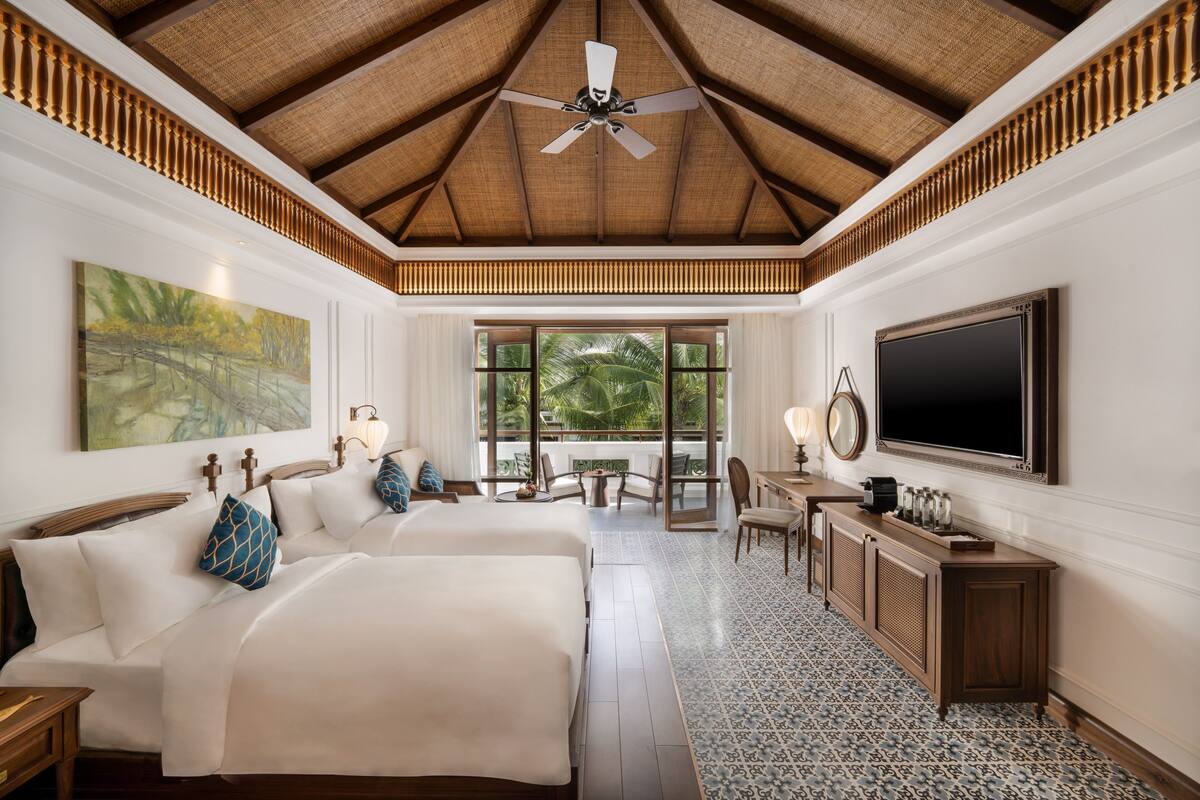 A hotel room with two beds, a large window with a view of palm trees, a ceiling fan, and a flat-screen TV.