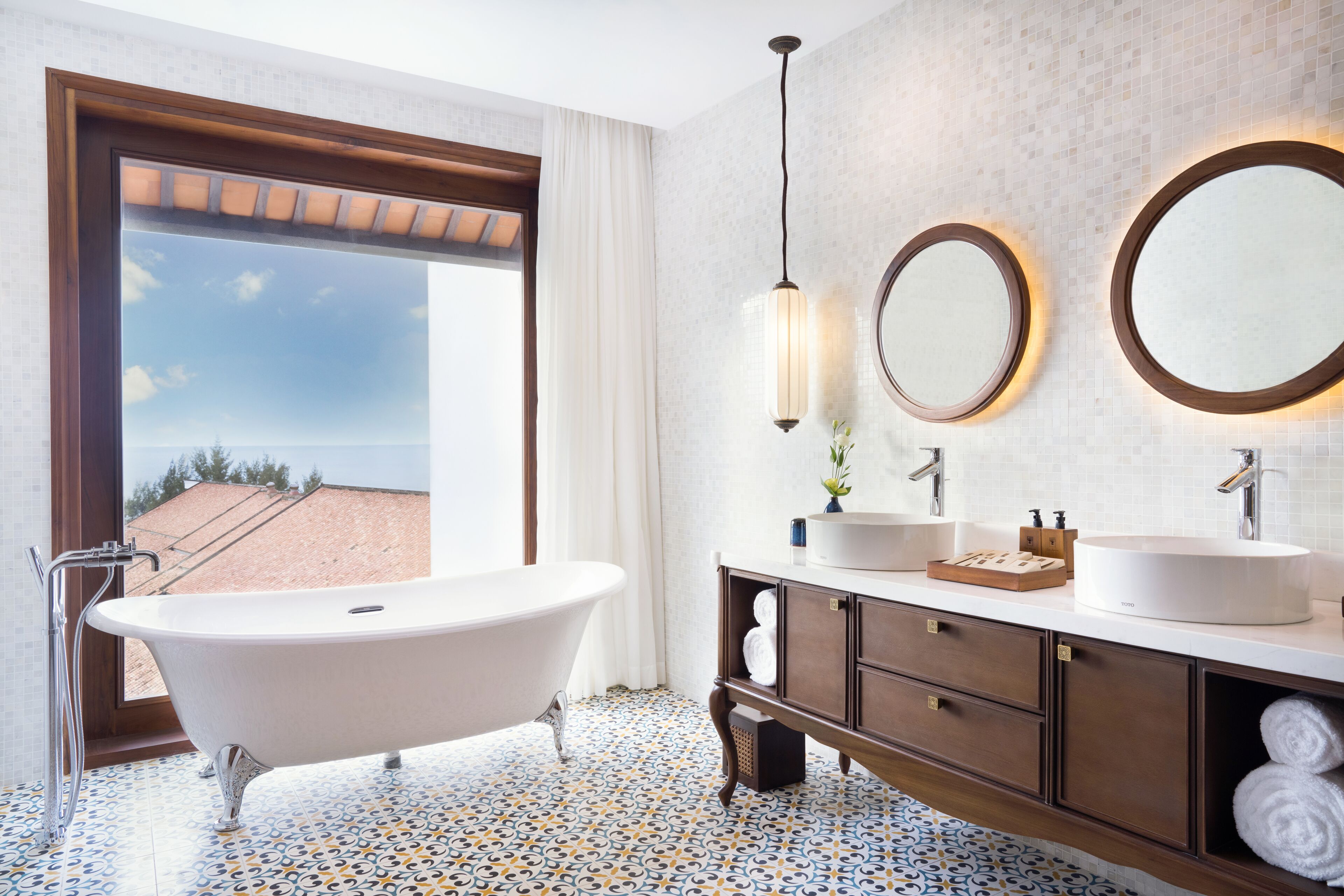 A bathroom with a freestanding bathtub, two sinks, a large mirror, and a view of the beach through a large window.