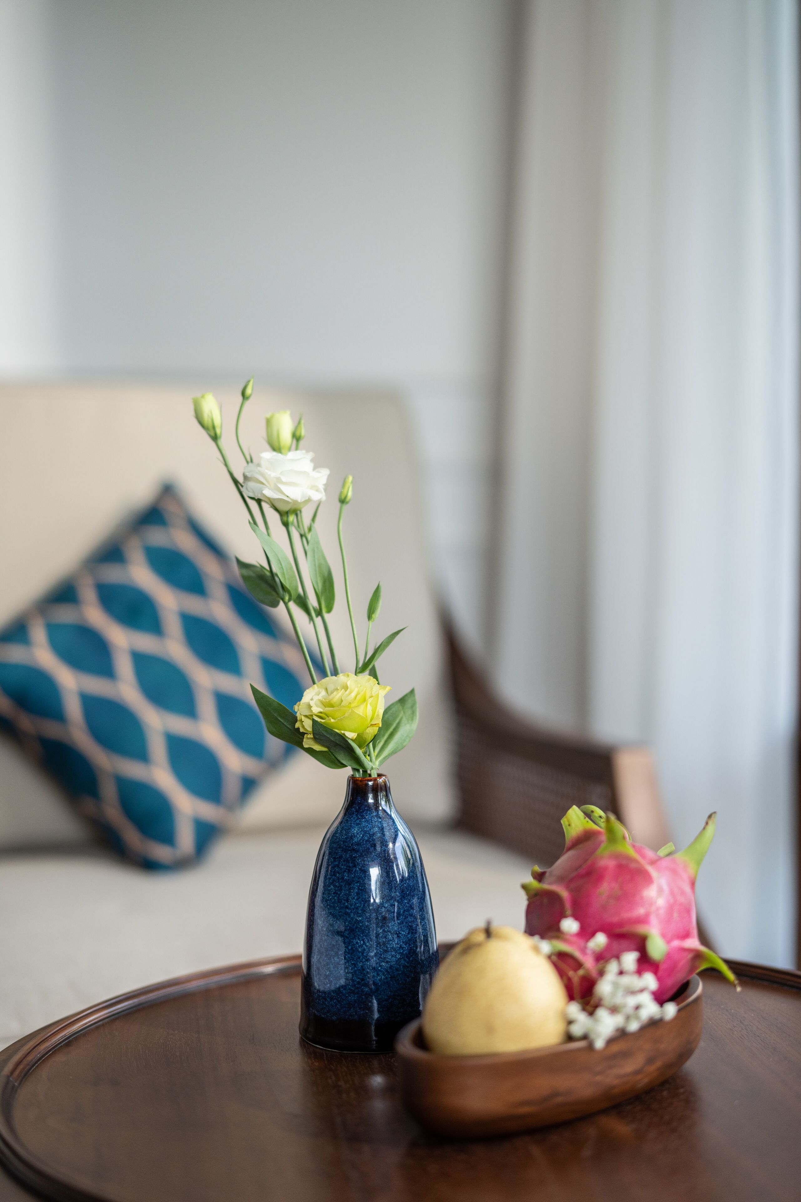 Una mesa con un jarrón de flores y un cuenco de madera que contiene una fruta y un pitahaya.