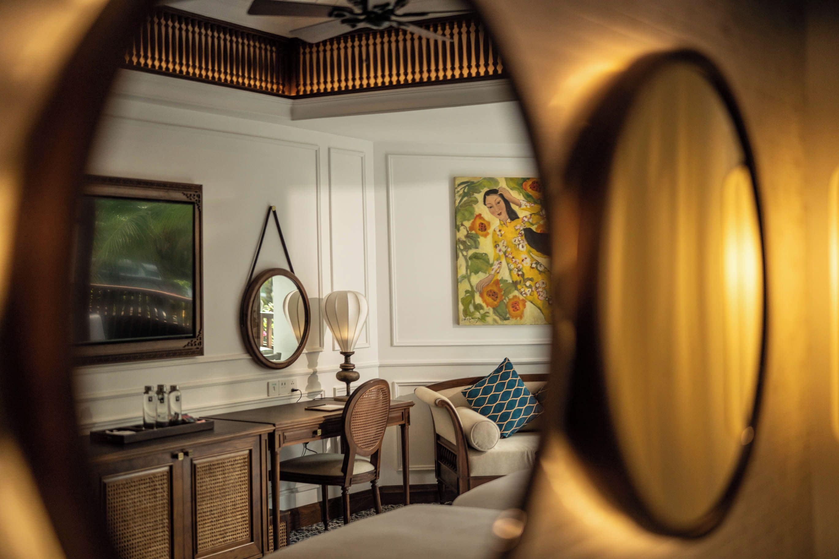 A room with a bed, a desk with a chair, a mirror, and a painting on the wall.
