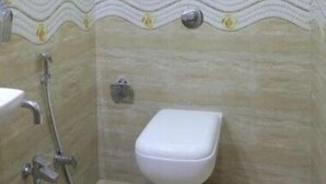 A small, tiled bathroom with a toilet, a shower, and a towel rack. - Hotel Golden Inn (Mumbai)