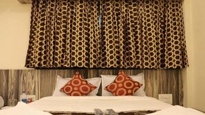A hotel room with a bed, two pillows with circular patterns, a wooden headboard, and a patterned curtain. - Hotel Golden Inn (Mumbai)