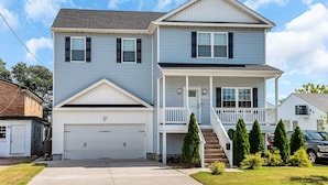 A two-story house with a front porch, a garage, and a driveway. - 4BR Spacious Retreat • Walk to Beach • Pets OK (Norfolk)