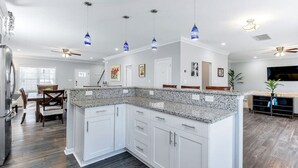 A modern kitchen with white cabinets, granite countertops, pendant lights, and a dining area with wooden chairs and a table. - 4BR Spacious Retreat • Walk to Beach • Pets OK (Norfolk)