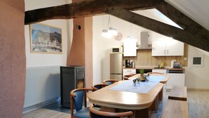 A dining area with a long wooden table, blue upholstered chairs, and a kitchen in the background.