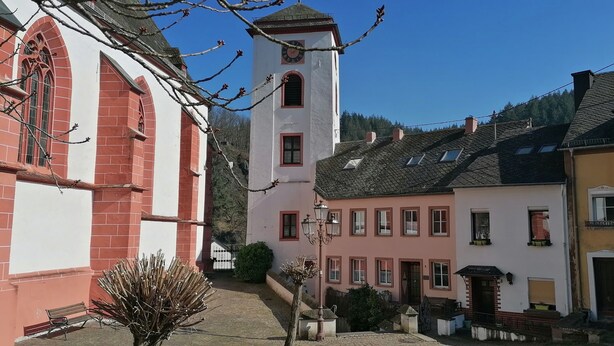 A traditional European town with a prominent church tower, a cobblestone street, and quaint buildings with uniform architecture.