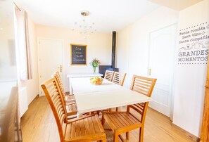 Un comedor con mesa blanca y sillas de madera, un jarrón con flores y una pizarra con un mensaje de bienvenida.