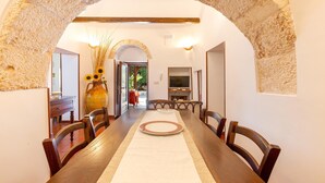 A dining area with a long wooden table, chairs, and a vase with sunflowers. - 2061 Villa Trulli Natura by Perle di Puglia (Noci)