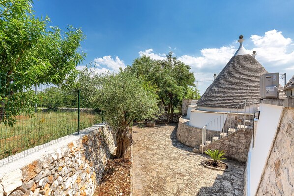 A stone pathway leading to a building with a conical roof, surrounded by trees and a stone wall. - 2061 Villa Trulli Natura by Perle di Puglia (Noci)