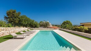 A rectangular swimming pool with clear blue water, surrounded by a stone wall and a grassy area with lounge chairs. - 2061 Villa Trulli Natura by Perle di Puglia (Noci)