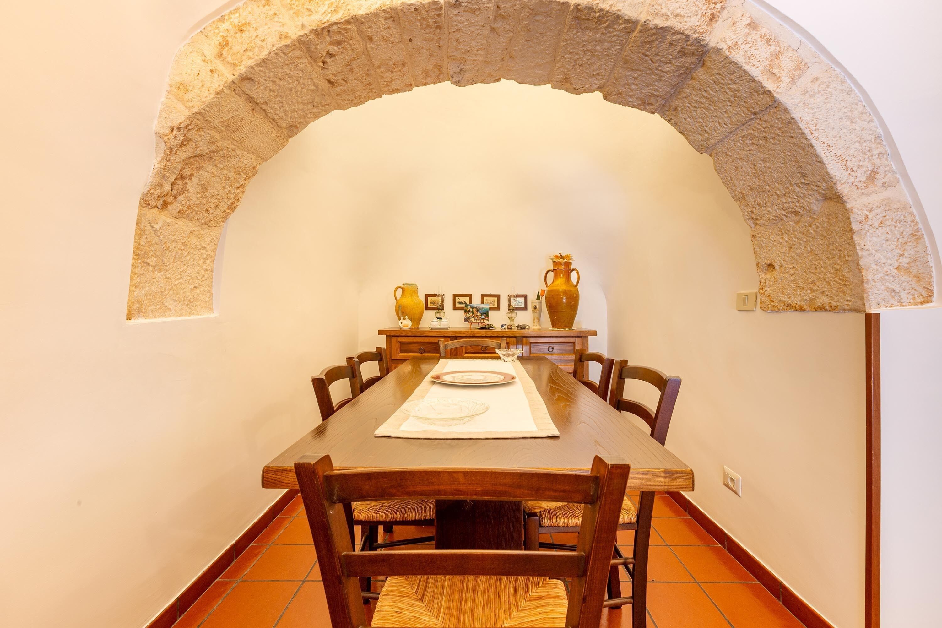 A dining area with a stone arch, wooden table, chairs, and a tiled floor.
