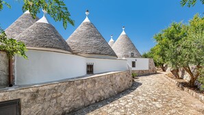 A pathway leading to traditional conical-roofed buildings with white walls and stone bases. - 2061 Villa Trulli Natura by Perle di Puglia (Noci)