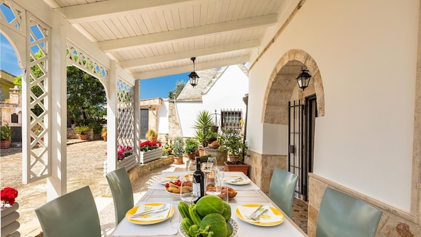 An outdoor dining area with a white pergola, stone walls, and potted plants. - 2061 Villa Trulli Natura by Perle di Puglia (Noci)