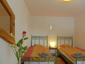 Une chambre avec deux lits simples, un miroir et un vase contenant une rose.
