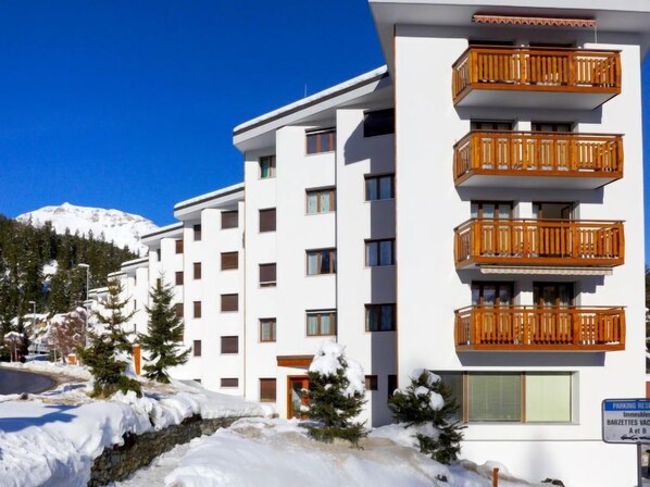 Un hôtel à plusieurs étages doté de balcons, un paysage enneigé et une montagne en arrière-plan.