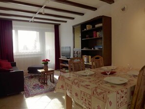 Un salon comprenant un canapé, un téléviseur, une bibliothèque et une table à manger mise avec des assiettes et des verres.