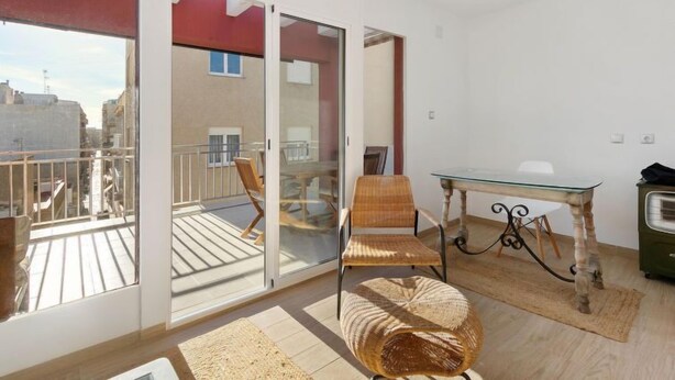 Ein Zimmer mit Glastür, die zu einem Außenbalkon führt, einem runden Korbsessel, einem Glastisch und einem Heizkörper.