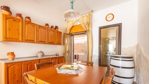 A wooden dining table with chairs, a kitchen area with wooden cabinets and a countertop, a large white barrel, and a clock on the wall. - 3032 Casa di Ada by Barbarhouse (Manduria)
