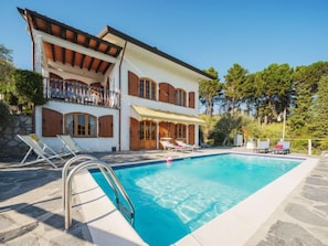 Un bâtiment à deux étages doté d’une piscine, d’un espace extérieur aménagé et d’un mur en pierre.