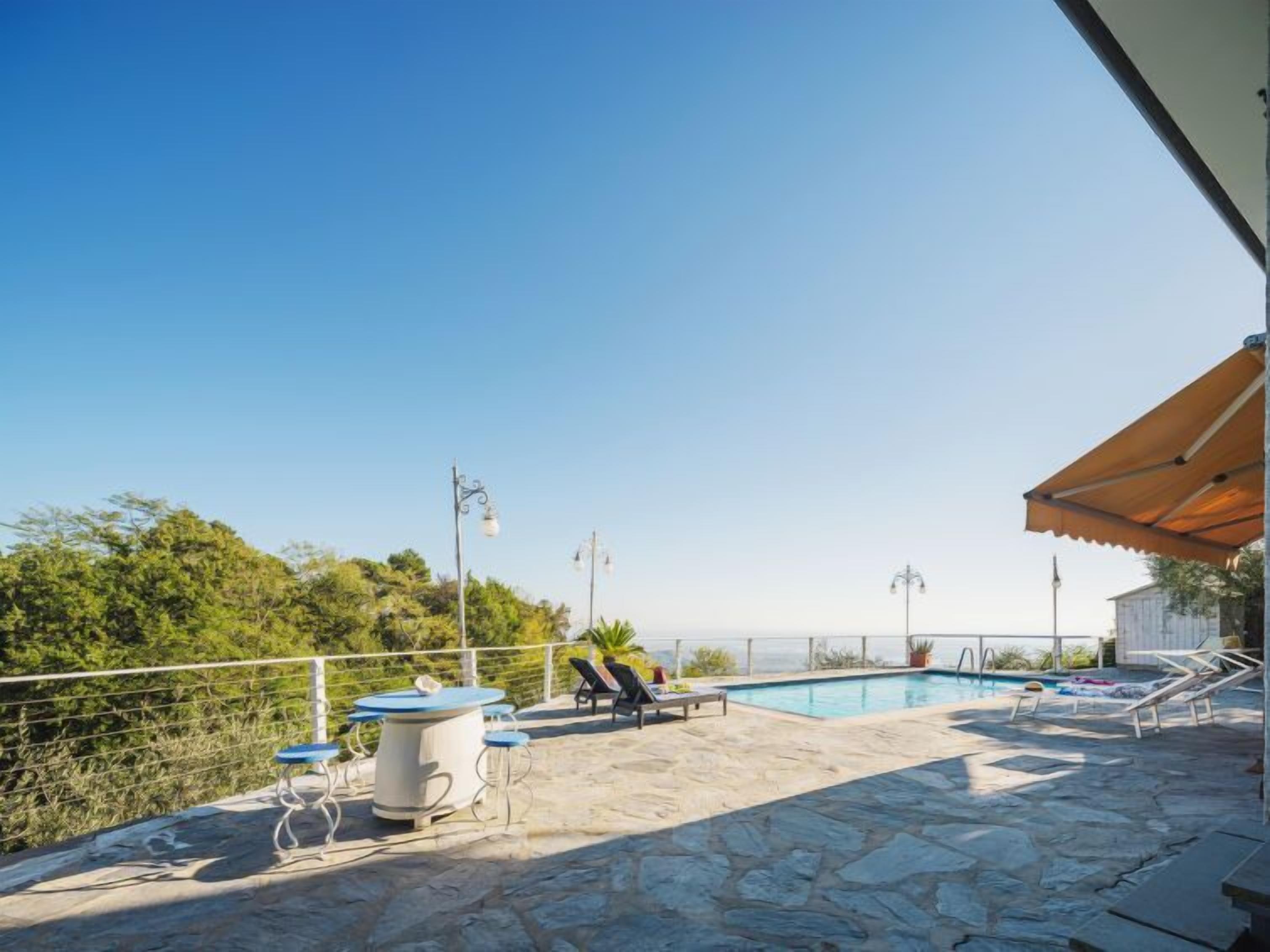 Área de piscina no terraço com espreguiçadeiras, mesa e vista para o mar.