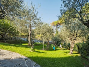 Un jardin bien entretenu, avec un chemin de pierres, une pelouse verdoyante et des arbres adultes.