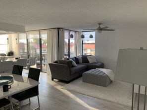 Un salon moderne avec un canapé gris, une table à manger blanche et une grande fenêtre agrémentée de rideaux.